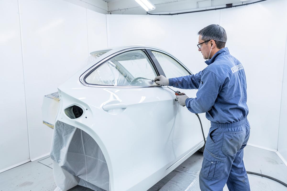 Carrossier peintre travaillant une portière en cabine de peinture
